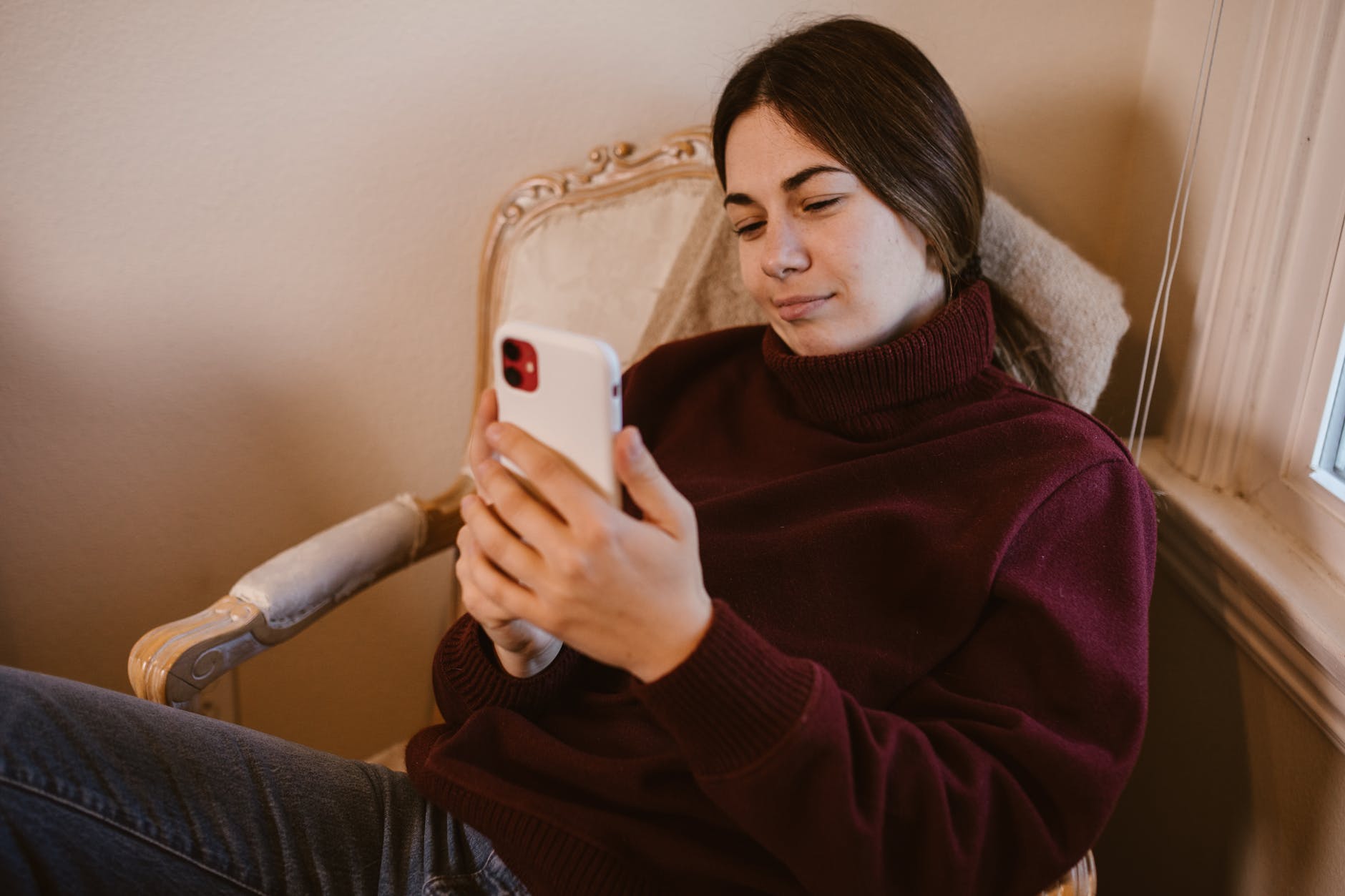 woman in maroon sweater holding white smartphone