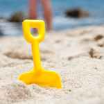 yellow shovel half buried on sand near the ocean