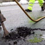 Road maintenance worker using asphalt to fill a pothole on a local road.