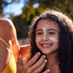 Woman applying sunscreen to a young child outdoors, highlighting the importance of sun safety and skin cancer prevention.