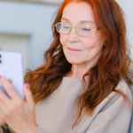 elderly woman with red hair in eyeglasses making video call
