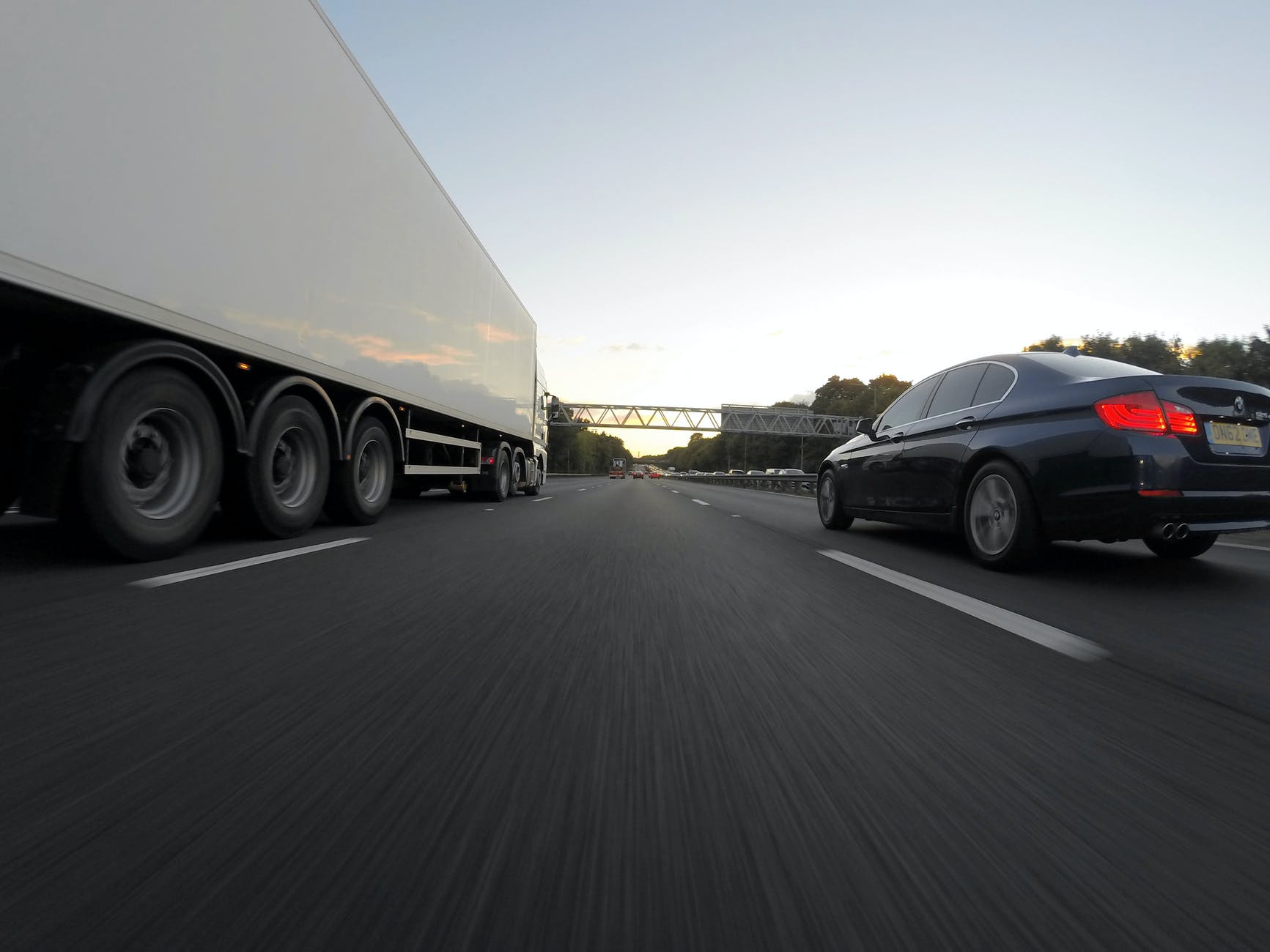 blue infiniti sedan running on road togerther with white freight truck