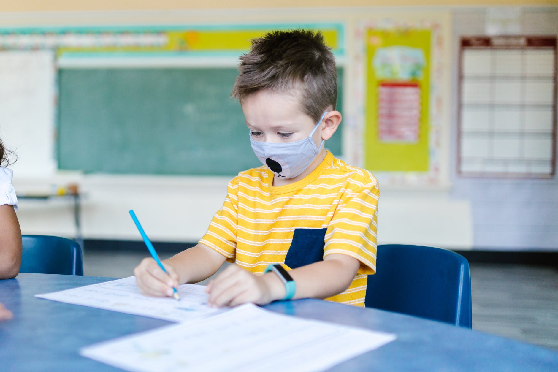 boy in yellow and blue striped t shirt and face mask drawing on white paper