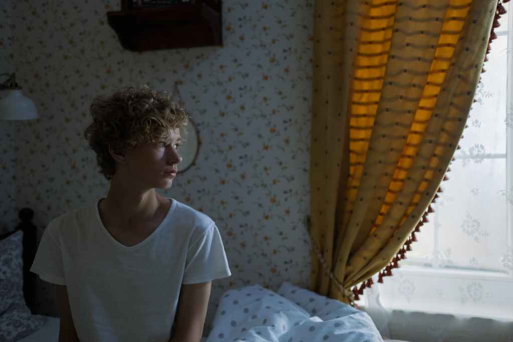 blond teenage boy sitting on bed