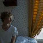 blond teenage boy sitting on bed