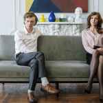 woman in white dress shirt and black pants sitting on gray couch