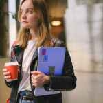 photo of a young woman holding a coffee cup and a laptop and looking away