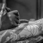 grayscale photo of person applying tattoo