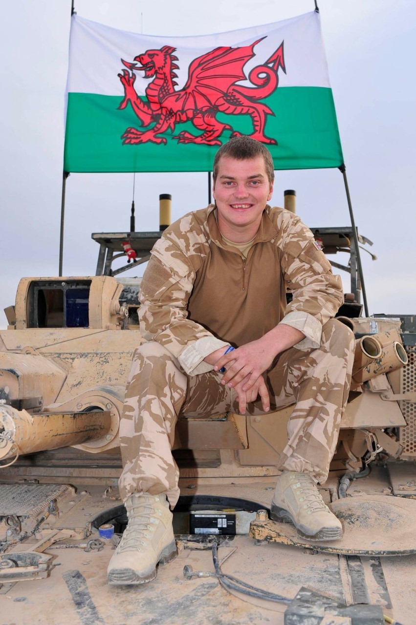 Dean in camo in front of Welsh flag