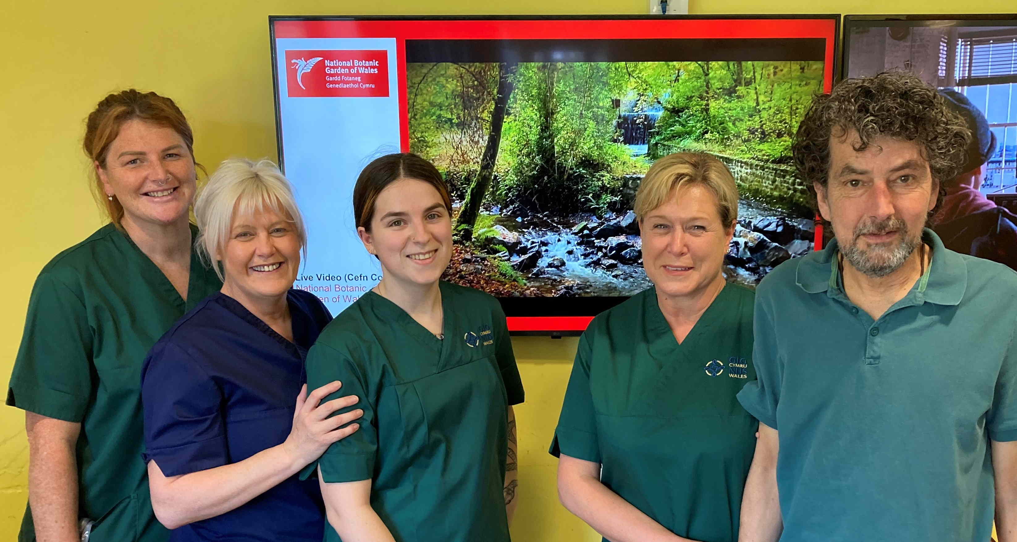 Cefn Coed staff Kellie Mills, Deborah Morgan, Jessey Cannings and Tracey Clarke with patient Roderick Brown in front of the hospital's live stream from the National Botanic Garden of Wales.