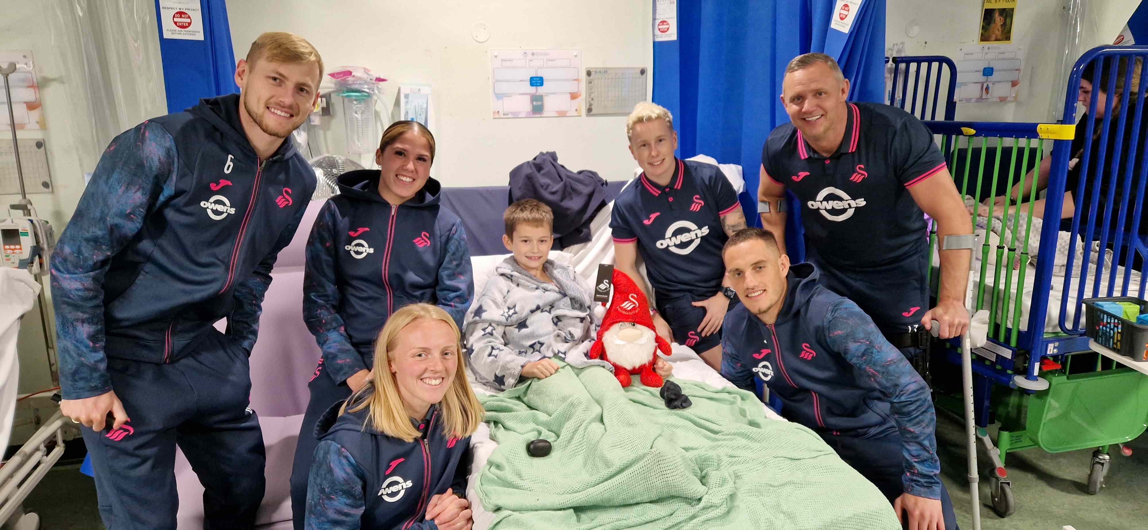 Riley Jenkins, 10, was visited by Swansea City players (back row, from left) Harry Darling, Jess Williams, Stacey John-Davis and club ambassador Lee Trundle along with Sophie Brisland-Hancocks and Jerry Yates. (Image: Swansea Bay NHS)