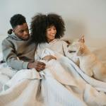 smiling young black couple petting curious dog on bed