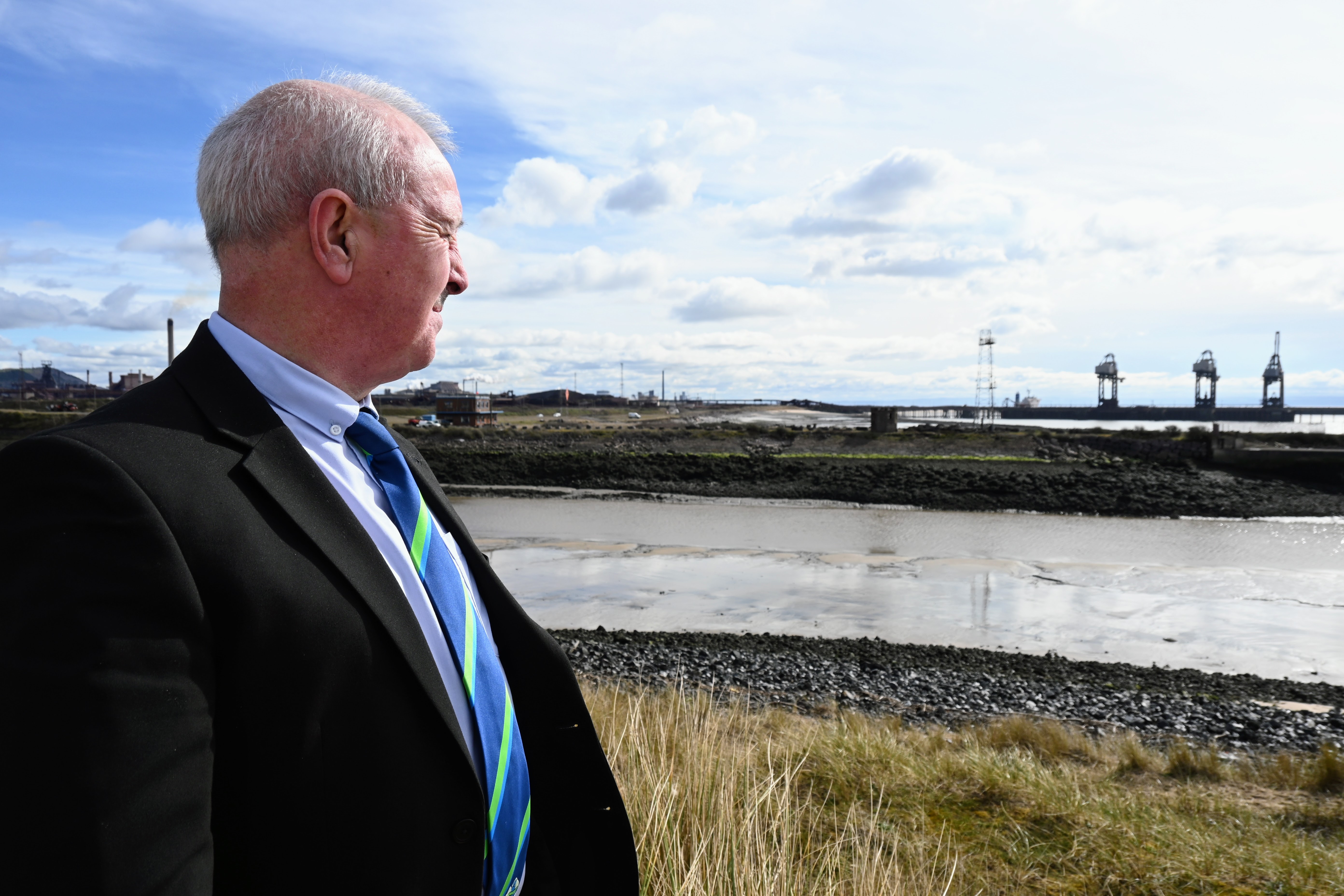 Council leader Steve Hunt stands on a hillside overlooking Port Talbot Steelworks in the distance, symbolising the community’s transition after the closure of the blast furnaces.