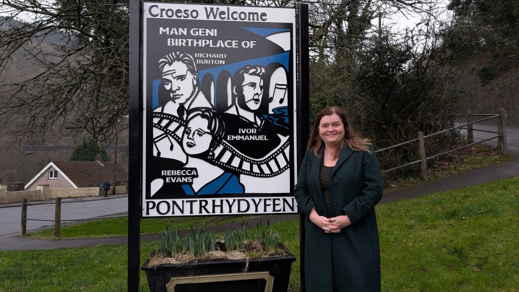 Sioned Williams besides the sign for Pontrhydyfen