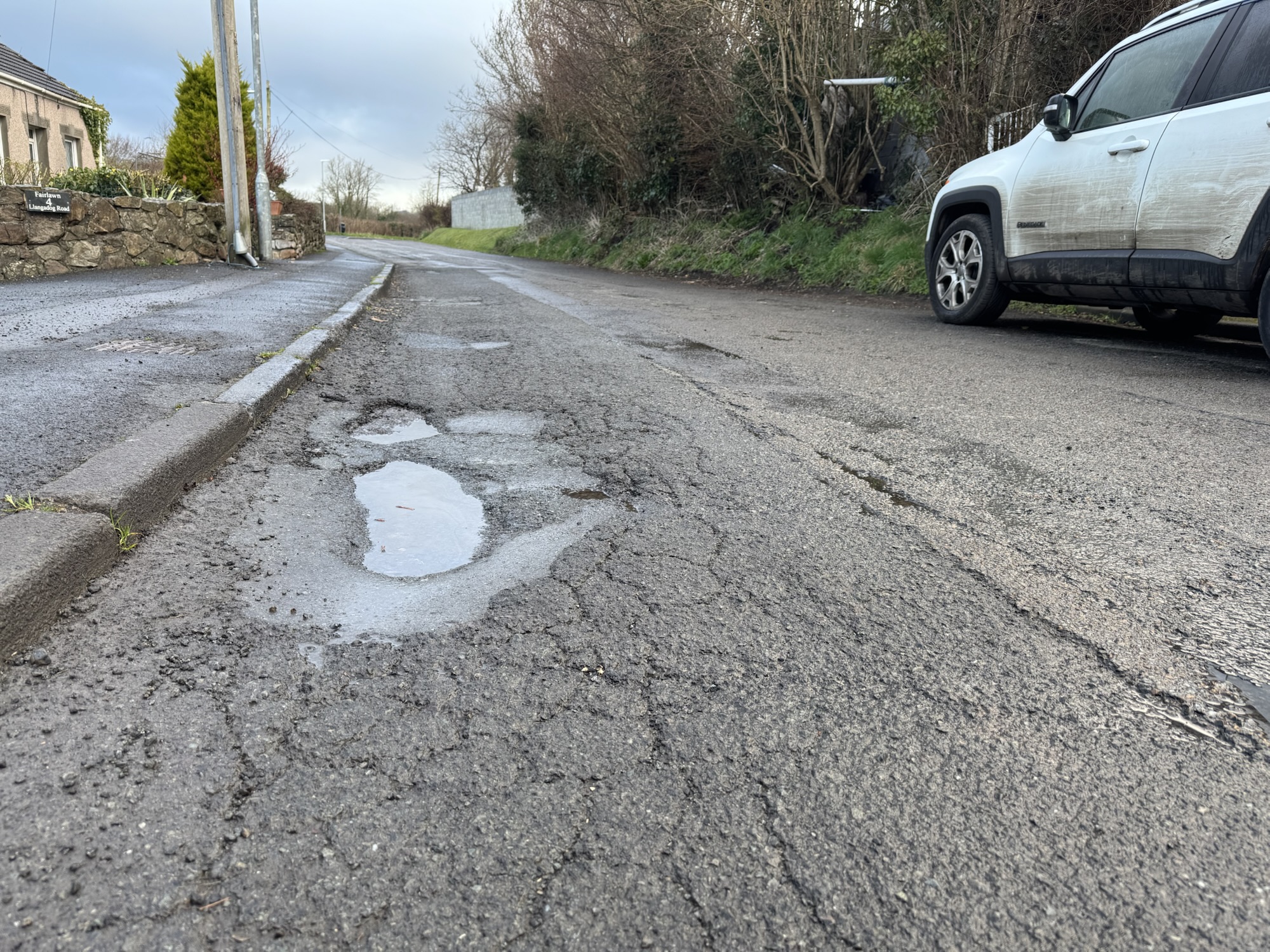 Large pothole on a country lane in South West Wales, highlighting the challenges of maintaining rural roads.