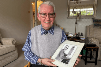 David at home holding a photograph of his younger self in front of the Guildhall - one of Swansea's iconic clocks he once maintained