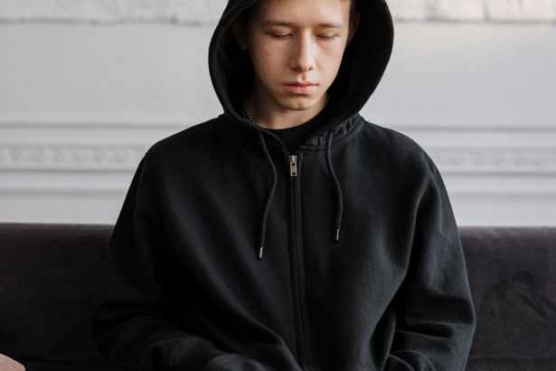 man in black hoodie sitting on brown couch