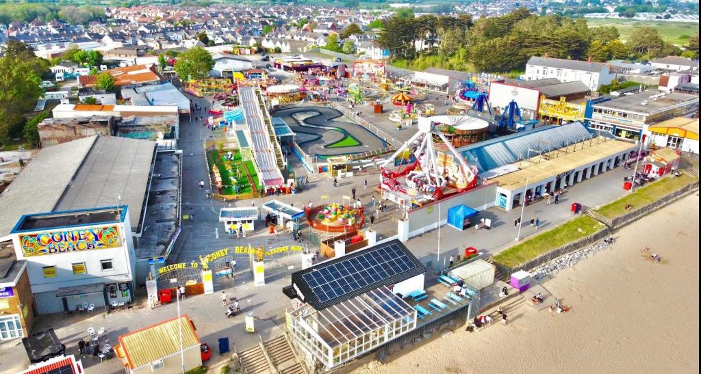 Aerial view of Coney Beach Pleasure Park in Porthcawl on a busy sunny day, with the Coney Beach sign and entrance arch, a go-kart track, a long slide and fairground rides beside the beach