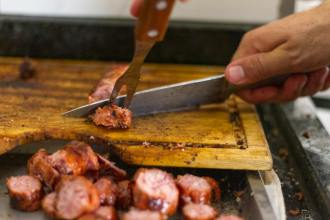 person slicing meat on wooden chopping board
