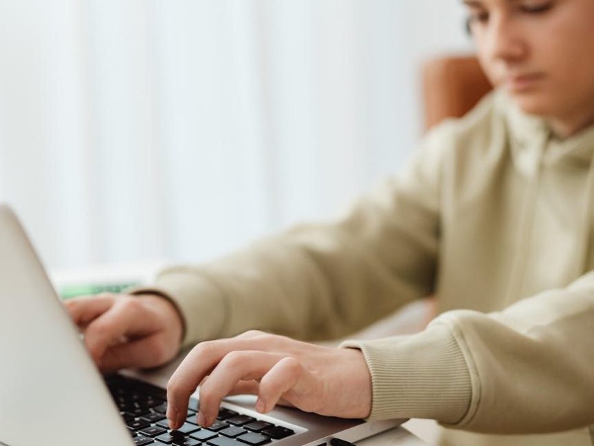selective focus photo of a boy typing on his laptop