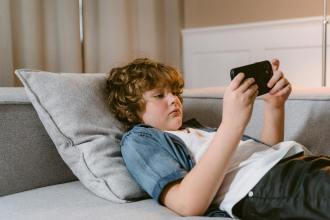 a boy using a smartphone while lying on a sofa