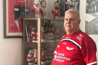 Llanelli mayor Andrew Bragoli stands in a Scarlets shirt in front of his memorabilia collection, showing his support for the Save Our Scarlets campaign.