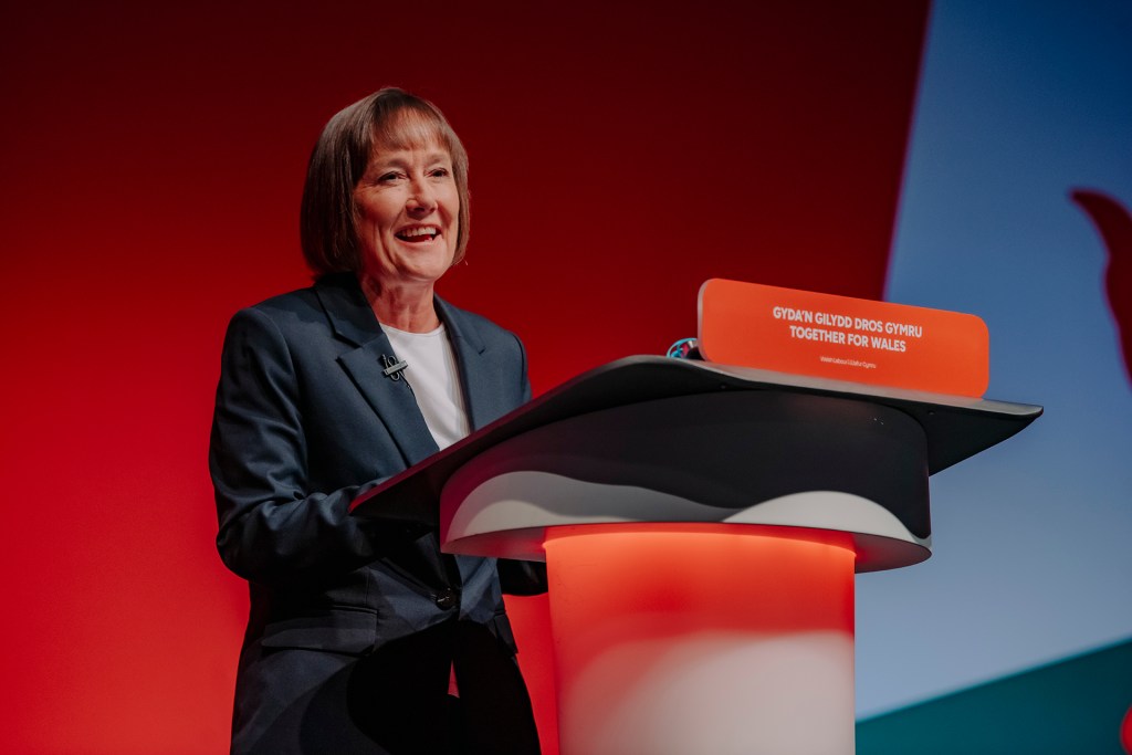 Jo Stevens speaking at the Labour Party conference lectern, setting out UK Labour’s support for Wales through investment in jobs, transport and high street renewal.