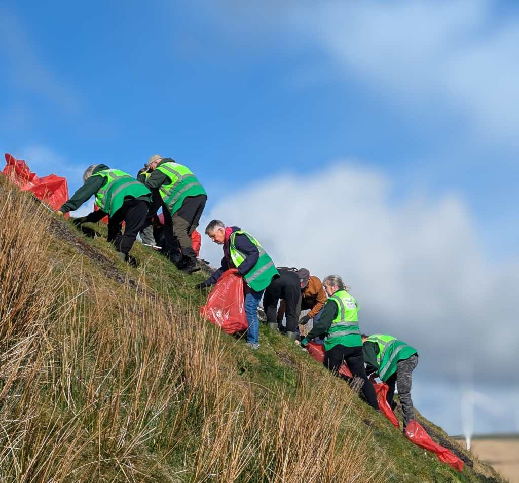 A close‑up of eight volunteers in high‑visibility vests collecting litter on a steep hillside in the Swansea Valley.