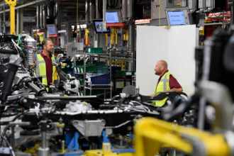 Two Jaguar Land Rover employees working on the Range Rover production line, wearing protective gear and assembling vehicles on the factory floor.