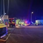 Night‑time scene showing ambulance, fire and police vehicles with blue lights at the B4304 roundabout near Llwynhendy, where crews used specialist equipment to rescue two people after a car left the road.
