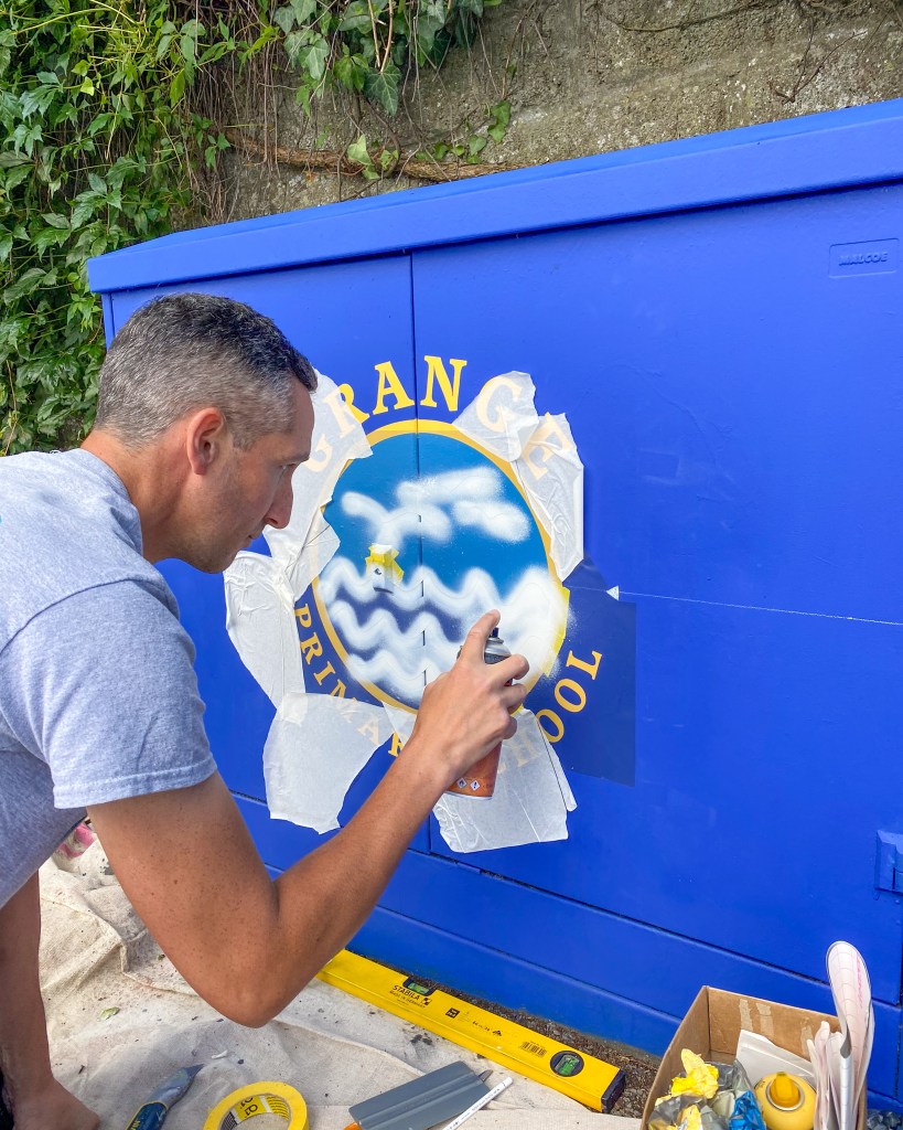 Artist painting a utility box mural in Swansea, part of a city‑wide project to brighten streets with community‑inspired artwork.