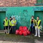 Five young people with litter pickers and rubbish bags standing in front of a graffiti wall in Port Talbot.