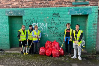 Five young people with litter pickers and rubbish bags standing in front of a graffiti wall in Port Talbot.
