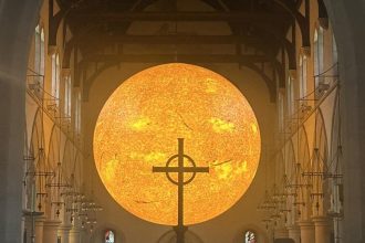 Helios, Luke Jerram’s giant Sun sculpture, shines behind the altar cross at Swansea Minster for Swansea Arts Weekend 2025.