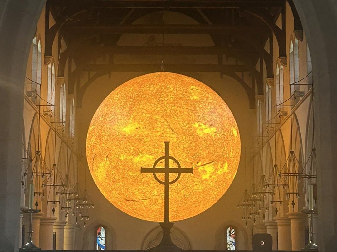 Helios, Luke Jerram’s giant Sun sculpture, shines behind the altar cross at Swansea Minster for Swansea Arts Weekend 2025.