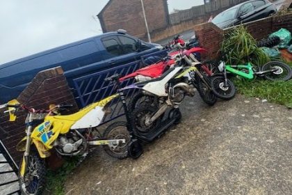 Several off‑road motorcycles lined up against a garden wall and gate after being seized by police in Blaenymaes.