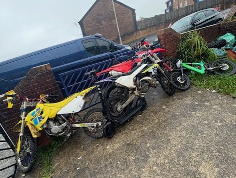 Several off‑road motorcycles lined up against a garden wall and gate after being seized by police in Blaenymaes.