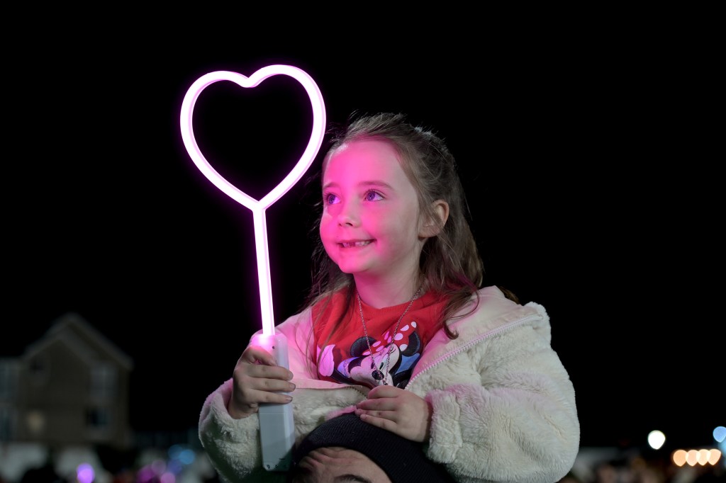 Smiling young girl holding a light‑up heart stick at Swansea’s fireworks display.