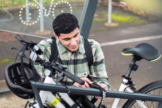 A man secures his bike to a rack at a Transport for Wales station, highlighting cycle parking facilities designed to support safer, greener travel.