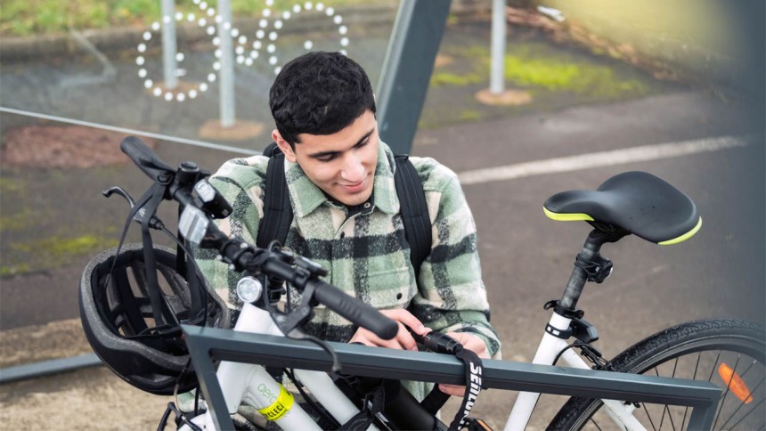 A man secures his bike to a rack at a Transport for Wales station, highlighting cycle parking facilities designed to support safer, greener travel.