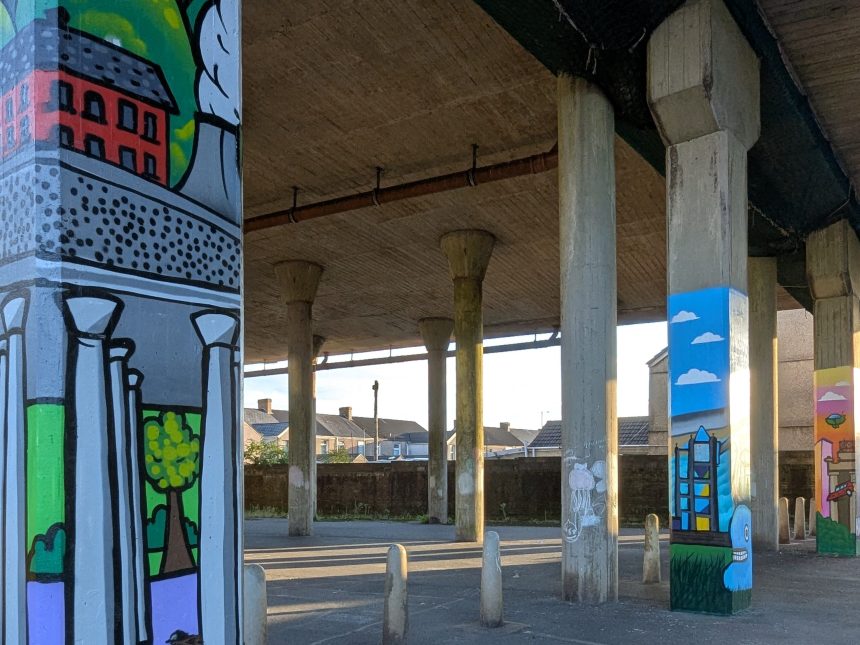 A wide view of colourful murals painted on concrete posts beneath the M4 flyover in Port Talbot.