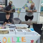 Seven‑year‑old Swansea fundraiser Ollie Blake smiling at his cake stall after cycling 15 miles to raise £1,600 for Faith in Families.