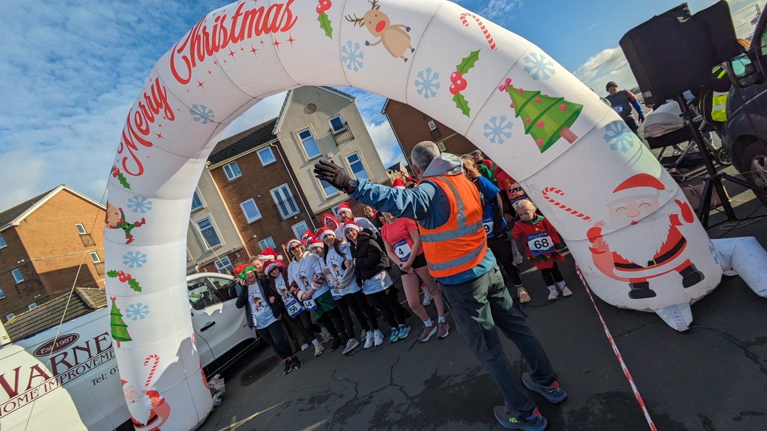 Front view of participants in elf hats and costumes gathered at the start line under the arch for the Mental Elf 5k in Aberavon.