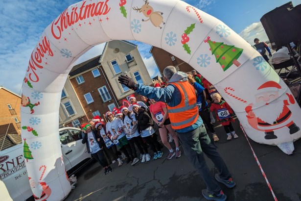 Front view of participants in elf hats and costumes gathered at the start line under the arch for the Mental Elf 5k in Aberavon.