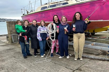 All‑female Pink Puffins crew standing together in front of their moored pink yacht.