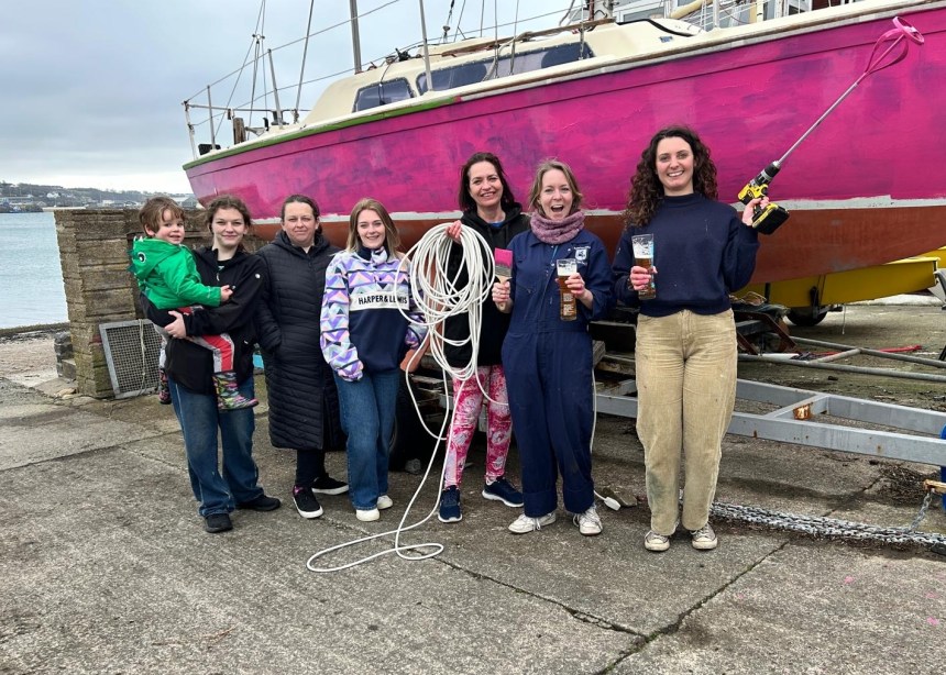 All‑female Pink Puffins crew standing together in front of their moored pink yacht.