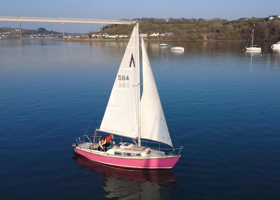 Wide shot of the Pink Puffins’ pink yacht sailing with crew on board.