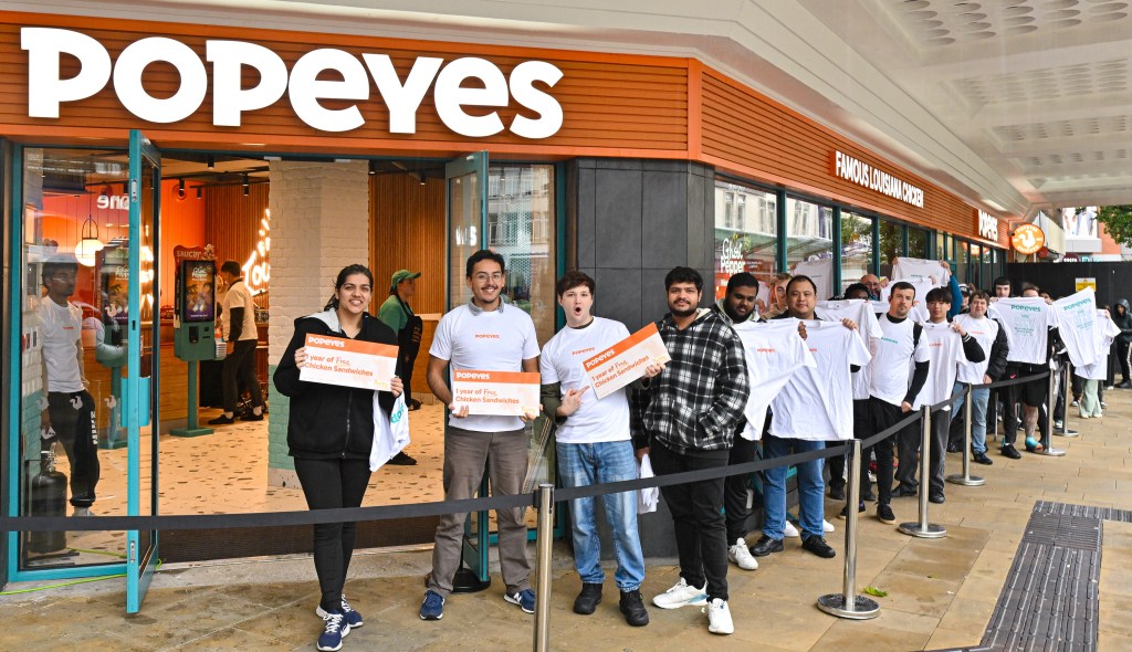 Three Popeyes superfans at the Swansea opening, celebrating with branded merchandise after winning a year’s free Chicken Sandwiches.