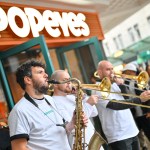 Musicians playing saxophone and trombones in a New Orleans‑style brass band outside Popeyes Swansea during the opening celebrations.