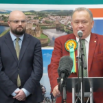 Screenshot from ITV News coverage of the Caerphilly by‑election showing Plaid Cymru’s winning candidate at the podium and Reform UK’s candidate beside him looking disappointed.